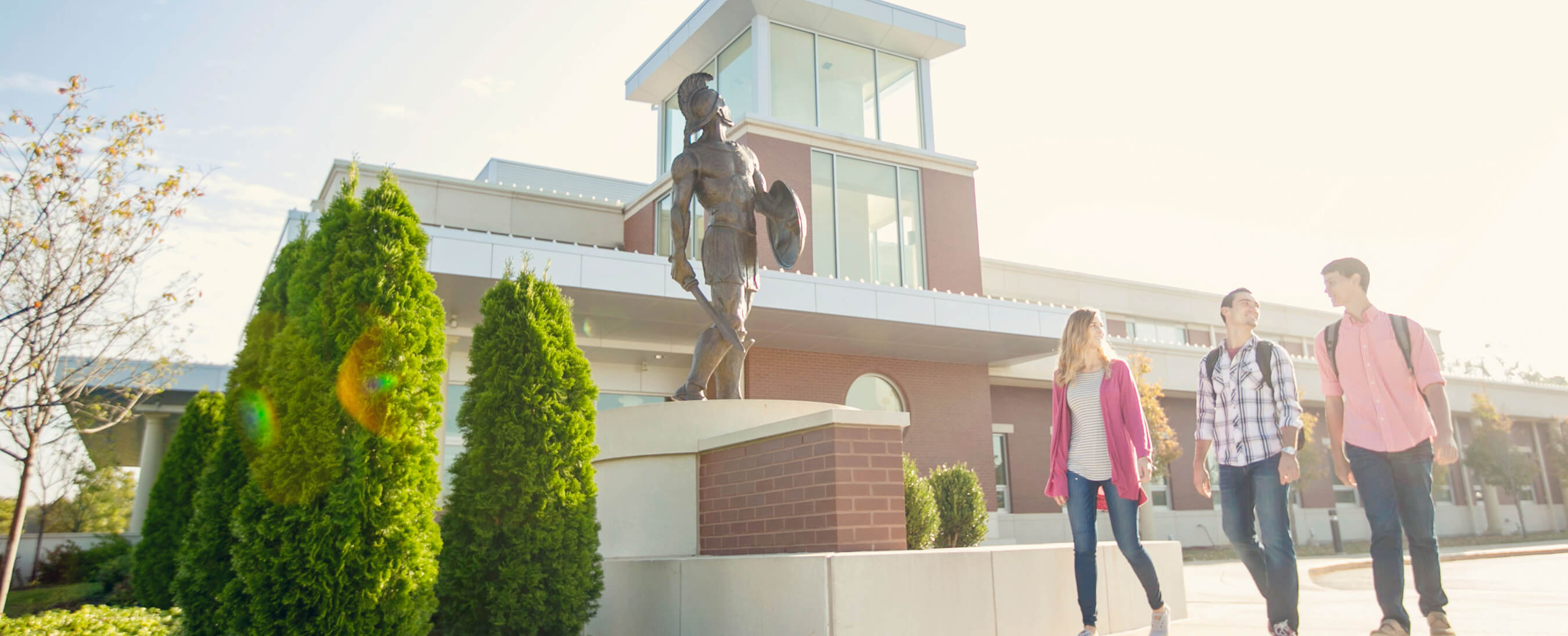 Students walking past MBU's Spartan statue on a bright day